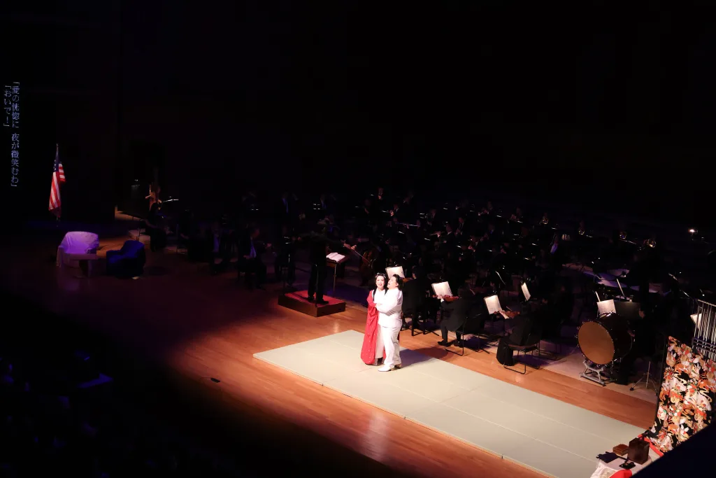 下手側に星条旗、上手に衣紋掛に広がる打掛が配置され、日本と米国の間で揺れ動く心理の象徴とした。その他、オペラ初心者の理解を助けるための工夫が随所に施されていた