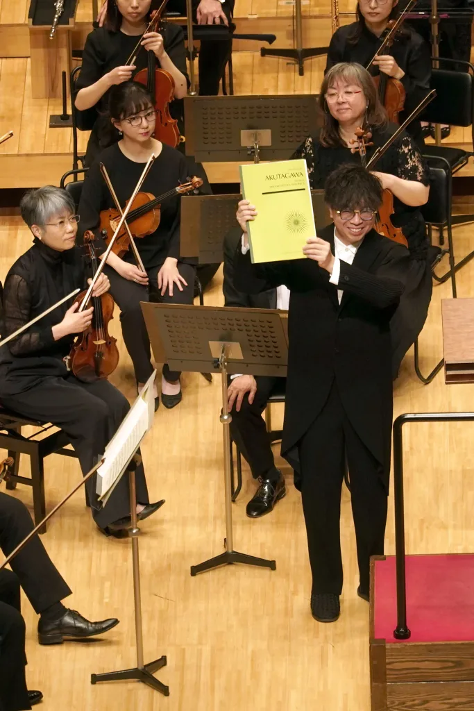 芥川也寸志「交響管絃楽のための音楽」のスコアを掲げるカーチュン　Ⓒ山口敦